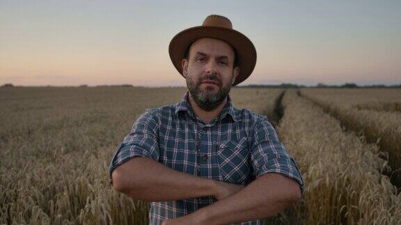 肖像白种农民男子在格子衬衫在帽子看着相机农田日落景观农业肖像农民戴着帽子站在麦田里农场工人日落的天空