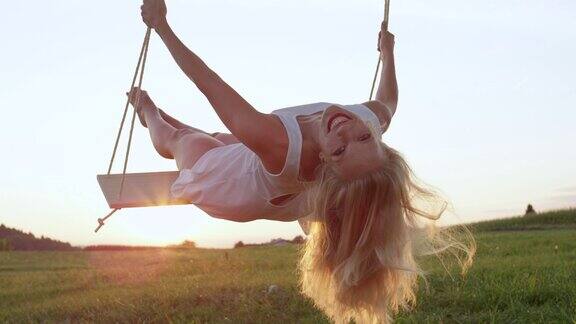 慢镜头特写:快乐的年轻女子微笑着在大自然中仰卧在秋千上