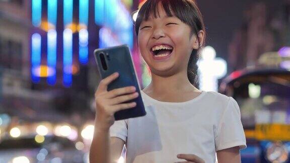 10岁的亚洲女孩晚上在城市里使用5G智能手机的幸福可视化5g