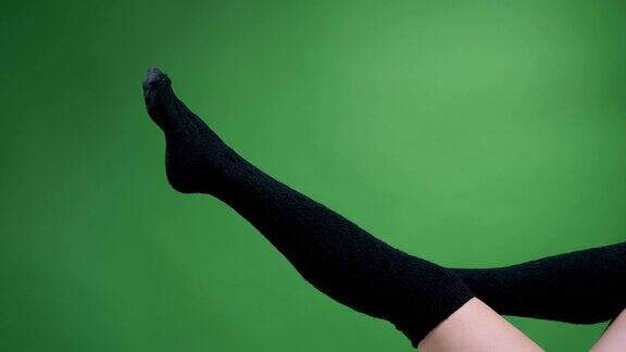 近距离拍摄的女性腿在可爱的黑色针织袜子与背景孤立在绿色