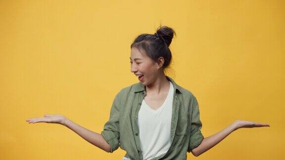 自信美丽的亚洲年轻女士站在孤立的黄色背景上张开手掌指向复制空间上的空白呈现广告微笑兴奋