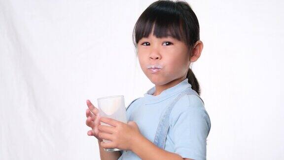 亚洲小可爱的女孩喝牛奶从一个杯子和舔她的嘴唇在白色背景的演播室为幼儿提供健康的营养