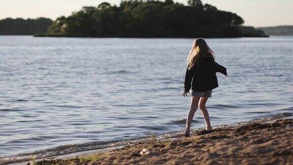 在落日的背景下美丽的女孩赤脚走在湖边