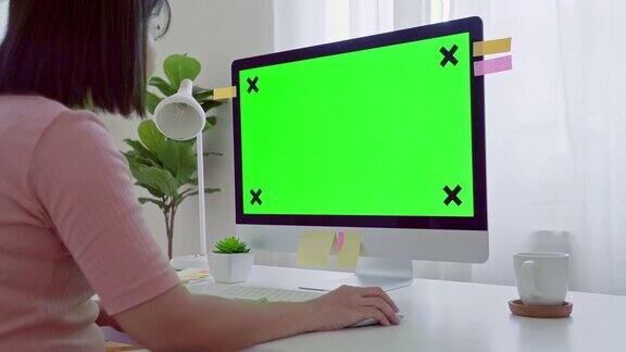 年轻的成年人在她的办公桌前工作在一台模拟绿色屏幕的电脑上过肩镜头她坐在家里的书桌前