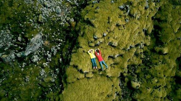 两名快乐的女游客躺在冰岛熔岩上的鸟瞰图直升机从近景飞到远景