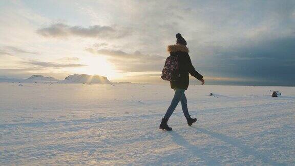 年轻美丽的女子旅行者走在冰岛的雪地沙漠上日落或日出时的慢动作拍摄在Solheimasandurdc3飞机坠毁区域附近