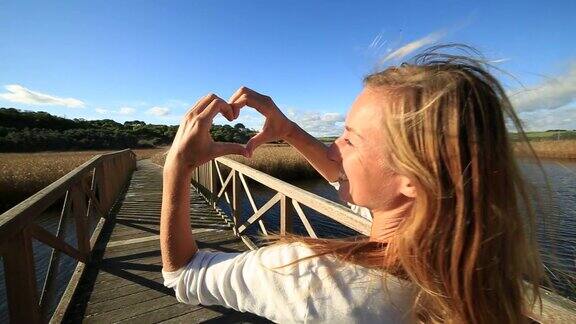 一个女人在湖上的桥上做心形的指架
