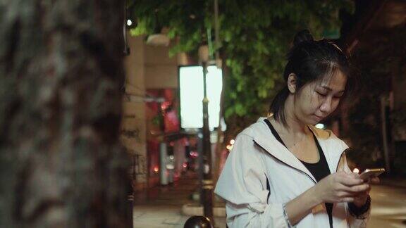 亚洲妇女在夜间城镇的街道上行走时使用手机