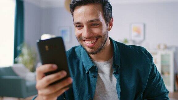 英俊微笑的男人在客厅放松时使用智能手机男人在网上浏览使用社交网络在家里玩
