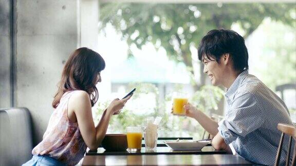 可爱的亚洲夫妇在咖啡馆与智能手机