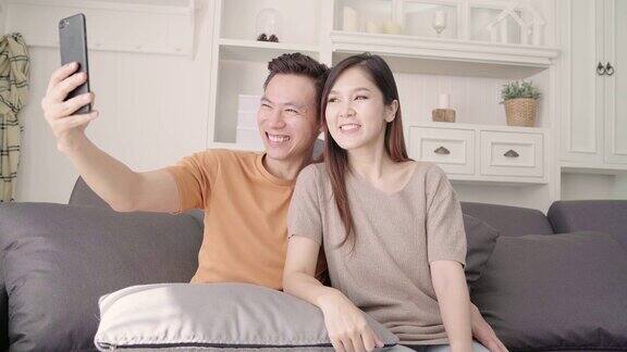 亚洲情侣在家客厅用智能手机自拍甜蜜的情侣躺在沙发上放松享受爱情时刻生活方式夫妇在家里放松
