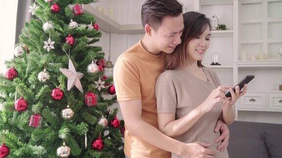 圣诞节亚洲夫妇用智能手机自拍和圣诞树装饰自家客厅生活方式女人和男人快乐庆祝夏天圣诞节和新年