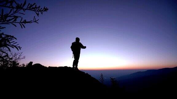 SLOMOMan站在山上对着日出的天空举起双臂
