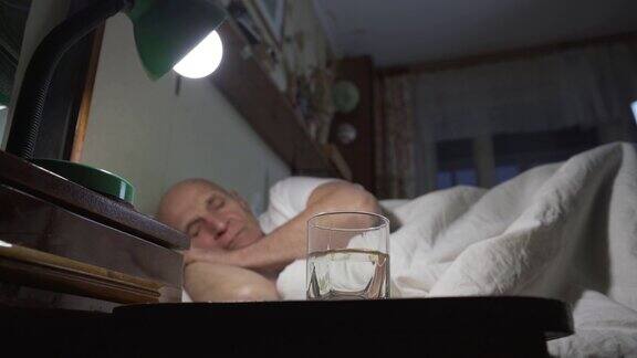 一位老人躺在床上盖着白毯子床头柜上放着一杯水