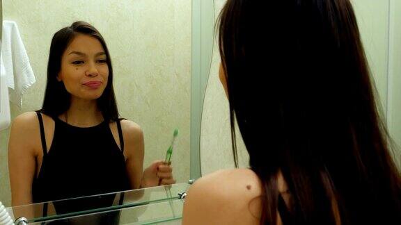 年轻漂亮的白人黑发女人一边刷牙一边对着镜子微笑