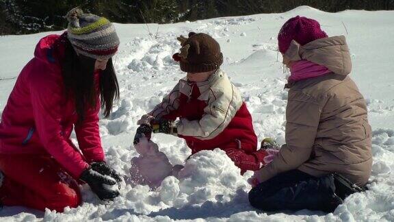 快乐的家庭在冬天的雪山森林里玩耍妈妈和她的两个孩子扔雪球做一个雪人他们笑了