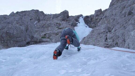 慢动作自下而上:女性冰上攀登者将她的冰爪踢入坚硬的冰上