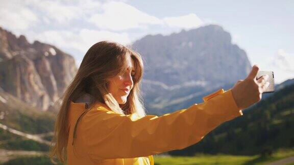 年轻开朗的女人穿着黄色雨衣自拍在美丽的山背景在阳光明媚的一天慢镜头