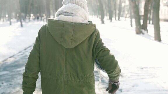 慢镜头后视图的女人在温暖的冬天的衣服走在下雪的冬天城市公园在寒冷的阳光灿烂的一天