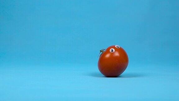 一个长着眼睛的红番茄在慢慢地滚动蓝色背景下的番茄卷缓慢的运动