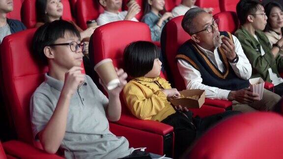 一位亚洲华人爷爷和他的孙子们喜欢在电影院看电影