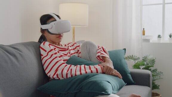 年轻女性戴着VR头戴式耳机在家中客厅观看电影体验模拟数字世界