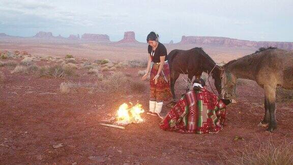 两个美国土著姐妹一个在打鼓裹着传统的纳瓦霍毯子在篝火旁取暖标志性的纪念碑日落