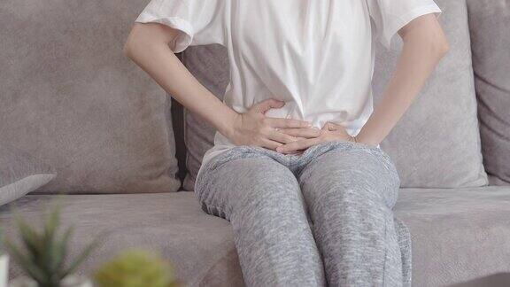 亚洲妇女有盆腔疼痛胃痛而坐在沙发上在她的家