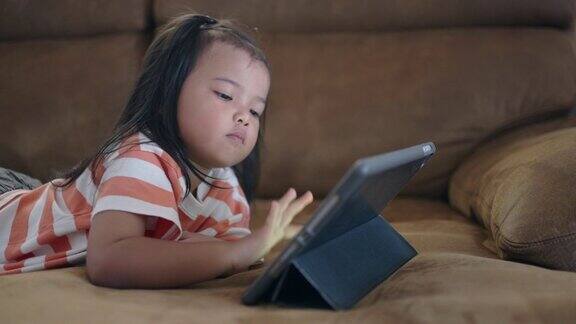 一个亚洲小女孩躺在沙发上喜欢看平板电脑