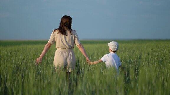 幸福家庭理念妈妈带着儿子走在草地上快乐的男孩牵着妈妈的手走在麦田里