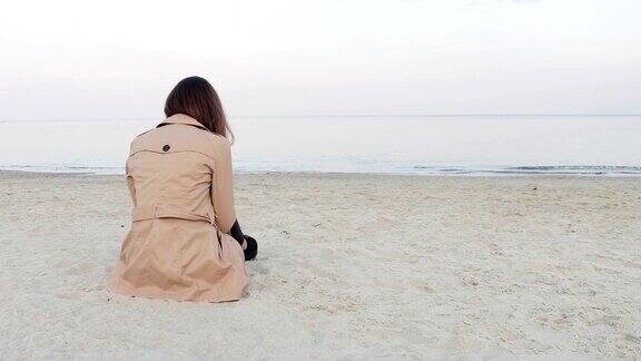 穿着米色外套的女人坐在海滩上从后面看