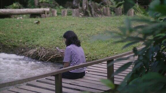 一个阳光明媚的日子年轻女子坐在森林瀑布上的木桥上