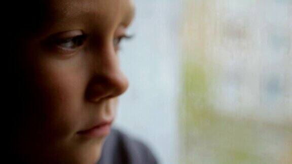 悲伤的男孩在雨天望着窗外