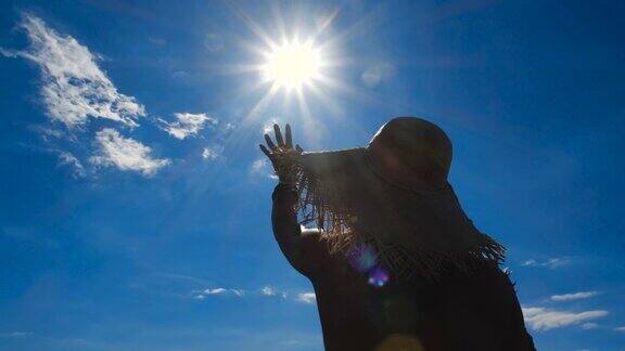 近剪影的美丽的年轻女子在草帽喝菠萝鸡尾酒和伸出她的手对太阳的背景蓝色的天空4k50fps慢动作