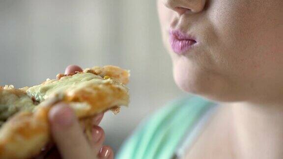 近距离的胖女孩咬披萨片快餐和超重