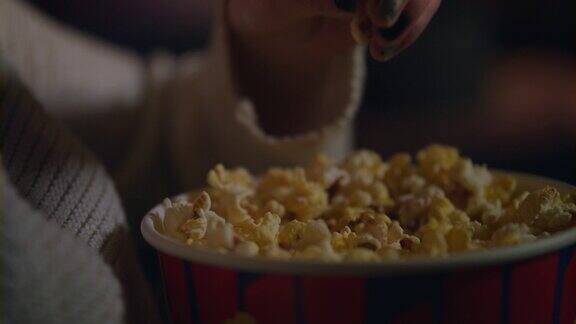 女性手从纸桶中采摘爆米花特写在电影院吃爆米花