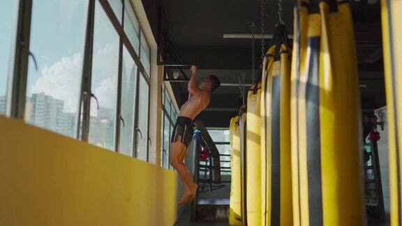 亚洲马来人运动员在健身俱乐部的窗户旁边用一排黄色沙袋做引体向上