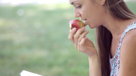 年轻女子在公园里一边看书一边吃苹果