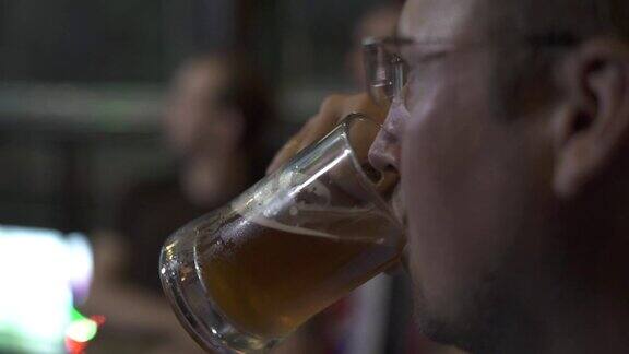帅哥喝啤酒从马克杯酒吧关闭肖像年轻人看起来运动比赛和喝冰啤酒在体育酒吧