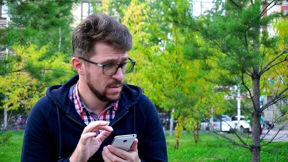 一名沮丧的中年男子坐在公园里用智能手机发信息