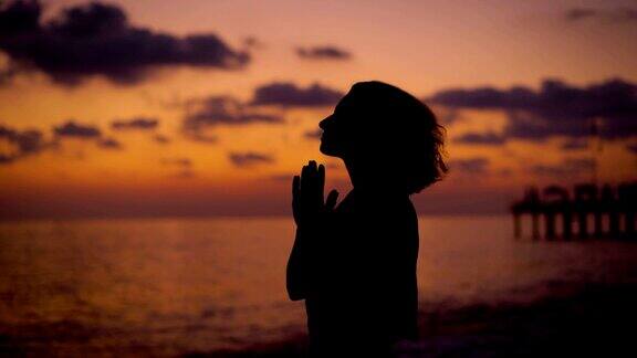 暮色中一个女人在海边举起双手祈祷