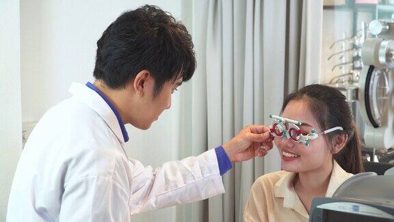 验光师在插入镜片后调整距离试镜架测试亚洲年轻女性的视力阅读视力表Snellen视力表准备制作眼镜表达积极的情绪微笑以获得更好的视力