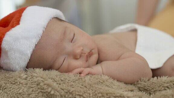 一个两个月大的亚洲新生儿躺在她的手掌上戴着圣诞老人的帽子睡在棕色的地毯上