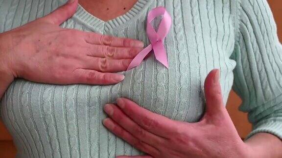 一个成熟女人的手在检查她的乳房粉红色的徽章丝带系在蓝色或薄荷色的针织毛衣上预防乳腺癌