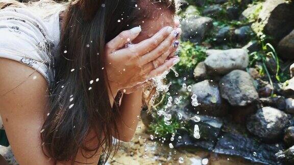 年轻女子在泉水中洗脸清澈的山溪
