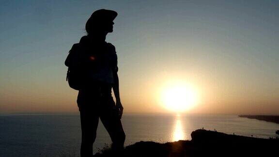 独立旅行的女人戴着帽子和背包从山顶欣赏日落