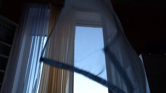 透明的蓝色和橙色的窗帘在开着的窗户前随风飞舞