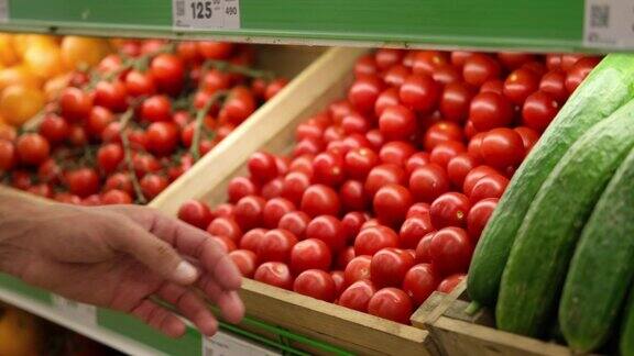 一个男人的手在挑选商店货架上的一个西红柿在市场上买蔬菜