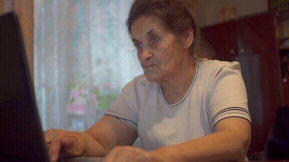 一位上了年纪的妇女坐在她公寓的笔记本电脑前她一边看显示器一边上网