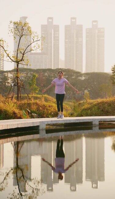 美丽的亚洲女性锻炼和慢跑在公园与城市建筑的背景